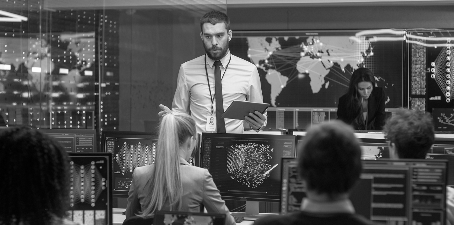 Man speaking to room full of people on computers. 